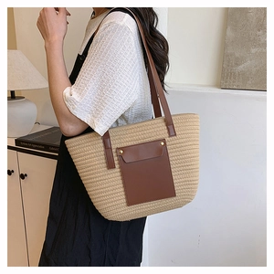 Close-up of woven straw tote bag featuring brown leather pocket and metallic stud details