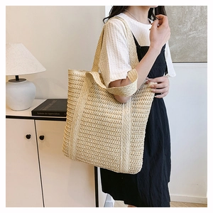 Close-up of a beige hollow-out woven straw tote bag worn over the shoulder