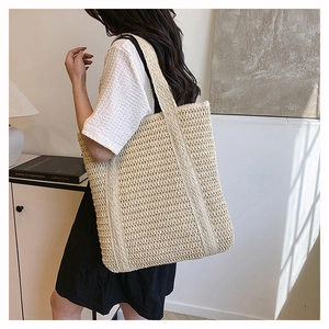 Detail of a beige woven straw tote bag featuring intricate grid texture and durable handle