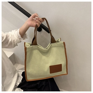 Close-up of green corduroy tote bag featuring leather handles and brown fashion tag