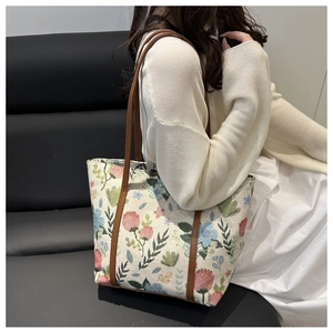 Detail of floral embroidery on beige tote bag worn with a white knitted sweater