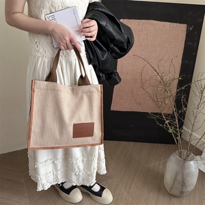 Fashionable beige corduroy tote bag with brown trim carried by a model in casual style