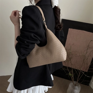 Minimalist beige crescent underarm bag with crocodile texture worn by model