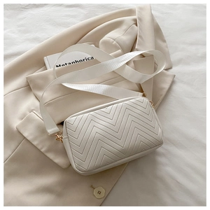 Close-up of white chevron quilted bag with gold hardware and wide fabric shoulder strap