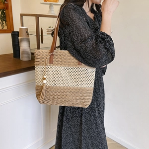 Fashionable woven straw tote bag with brown stripes and tassel, styled on shoulder
