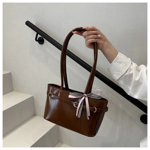Detailaufnahme der braunen PU-Tasche mit Metallringen und rosa karierter Schleife