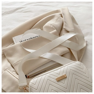 Detail of a creamy white crossbody bag with V-shaped quilting and golden metal buckle