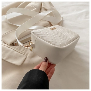 Detail of white quilted crossbody bag with golden hardware and wide fabric shoulder strap