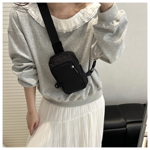 Close-up of a black waterproof nylon crossbody bag worn by a model in casual attire