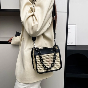 Detail view of woven straw shoulder bag featuring black chain and leather strap