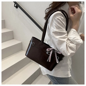 Dunkelbraune glänzende Schultertasche mit rosa karierter Schleife auf weißen Stufen