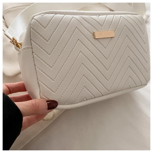 Detail of white quilted crossbody bag with V-shaped stitching and gold metal plate