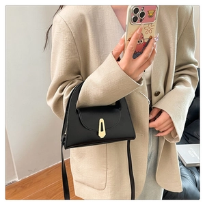 Detail of black semi-circular handbag with gold trapezoid metal clasp and leather strap