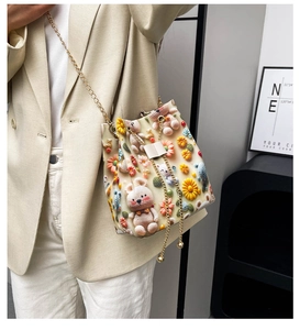 Détail du sac seau au crochet 3D avec fleurs, motif ours et chaîne dorée porté par un mannequin