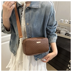Detail of V-quilted faux leather crossbody bag with wide textile strap and metal plate