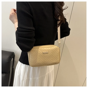 Detail of beige quilted crossbody bag with metal buckle and adjustable fabric shoulder strap