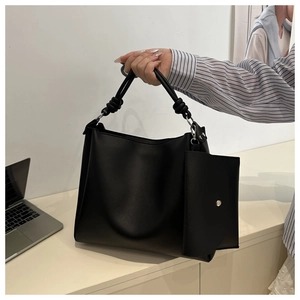 Detail of black leather tote bag with knot handle design and matching small pouch charm