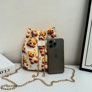 Vue détaillée du sac seau blanc avec motif d'ours 3D et chaîne dorée à côté d'un smartphone