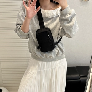 Minimalist black nylon chest bag with adjustable strap shown in a mirror selfie view