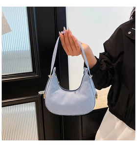 Close-up of a light blue textured crescent bag with stylish gold ring hardware detail