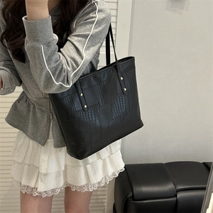 Black crocodile pattern tote bag with gold studs shown on shoulder for daily commute