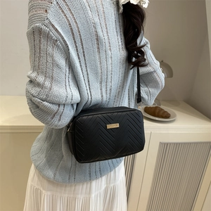Black quilted crossbody camera bag with gold hardware worn by a model in a casual setting