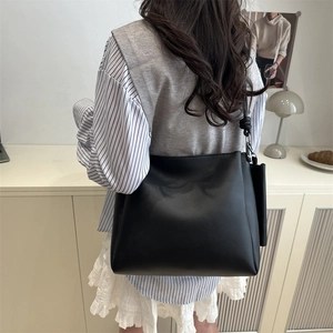 Retro black leather bucket tote bag with knot strap shown on shoulder by model