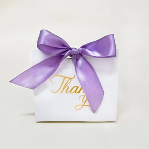 Detailed close-up of a white wedding gift box with a purple ribbon and gold Thank You text