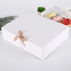 Große weiße Geschenkbox mit hellbrauner Schleife in einer gemütlichen Teestunde-Szenerie