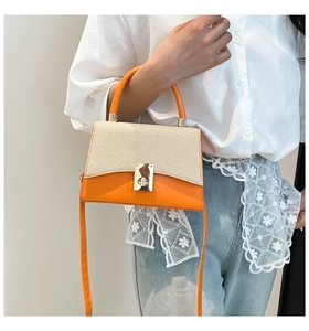 Détail des coutures contrastées, texture paille beige et bandoulière en cuir orange du sac