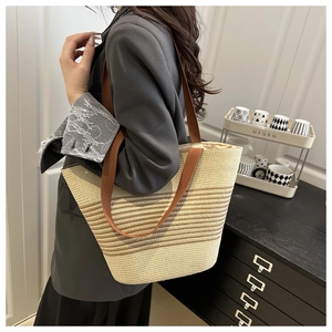 Detail of a large woven straw tote bag with brown stripes worn with a grey suit