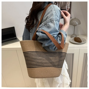 Detail of woven straw tote bag featuring black stripes and brown fabric strap