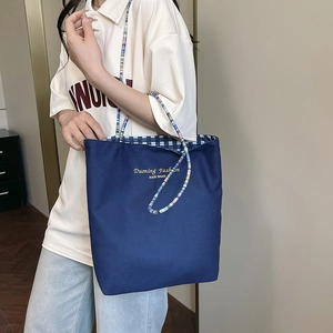 Blue canvas tote bag with colorful bead strap and classic plaid lining detail