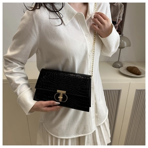 Detail of black crocodile texture bag with gold T-lock and chain strap on a model
