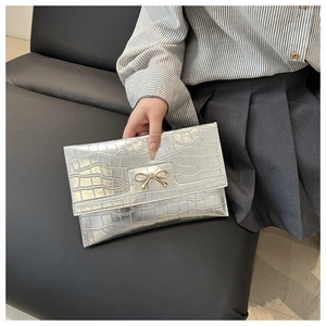 Silver crocodile texture envelope clutch bag with gold bow clasp in a hand-held view