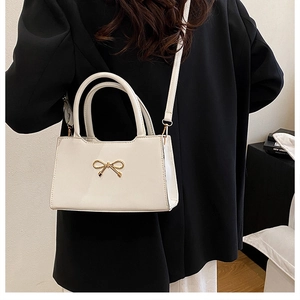 Détail d'un sac bandoulière blanc avec fermoir nœud doré porté par un mannequin chic