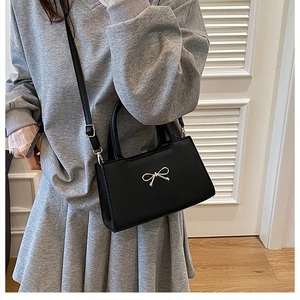 Détail du sac à bandoulière en cuir PU mat noir avec nœud doré et doubles poignées
