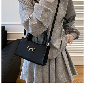 Détail d'un sac à main en cuir noir mat avec un nœud doré et une bandoulière amovible
