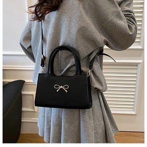Détail d'un sac bandoulière noir en similicuir avec nœud doré et bandoulière réglable