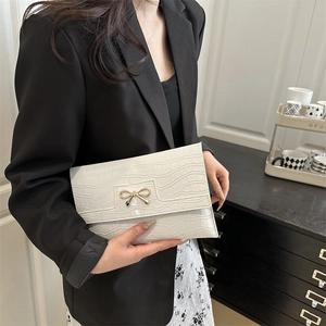 Chic beige crocodile embossed envelope bag with gold bow clasp held by a model