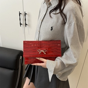 Red crocodile texture envelope clutch with gold bow lock held by a model in interior setting