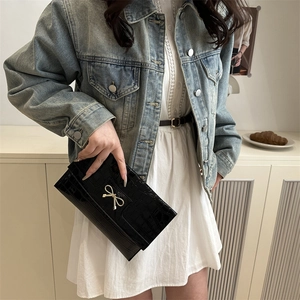 Black crocodile-pattern envelope bag with golden bow clasp worn with a denim jacket