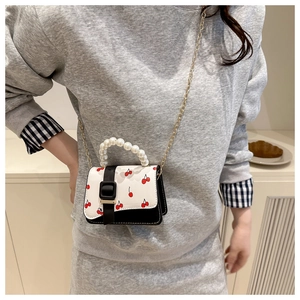 Détail d'un mini sac bandoulière imprimé cerise avec poignée perle et chaîne dorée