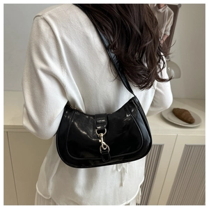 Détail d'un sac sous le bras en cuir verni noir avec boucle en métal doré porté à l'épaule
