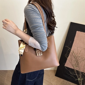 Brown leather tote bag with silk scarf on handle and metal buckle in lifestyle setting