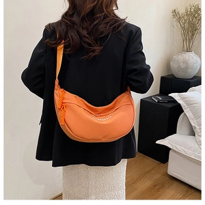 Detail of an orange crescent crossbody bag featuring a fashion logo and woven zipper pull