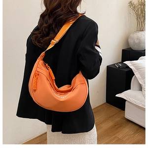 Detail of bright orange crescent crossbody bag with adjustable strap on model