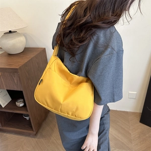Minimalist bright yellow nylon shoulder bag worn by model in a stylish indoor setting