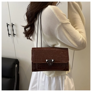 Détail d'un sac bandoulière marron effet crocodile avec boucle à rivets et chaîne métallique