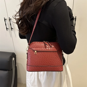 Sac bandoulière marron rouge à texture tissée et double fermeture éclair porté par un mannequin